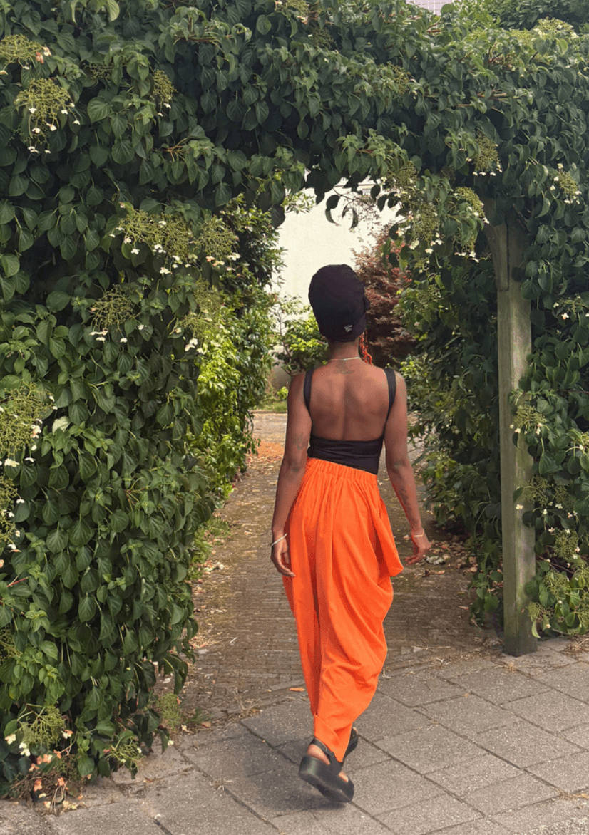 Presha Rivers loopt in een oranje broek door een groene bloemenboog, van achteren gezien